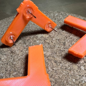 May include: Three orange plastic corner brackets with push pins. The brackets are designed to be used as corner protectors.