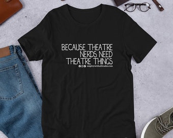 Puede incluir: Camiseta negra con texto blanco que dice "Because theatre nerds need theatre things" y una dirección de sitio web. La camiseta está colocada sobre una superficie gris con jeans azules, una cartera de cuero marrón, un reloj y unas gafas.