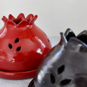 Puede incluir: Dos quemadores de incienso de cerámica, uno rojo y otro negro, con forma de granadas y recortes decorativos.