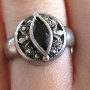 May include: A silver ring with a black gemstone surrounded by smaller silver stones.