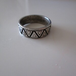 May include: A silver ring with a geometric pattern of black triangles around the band.