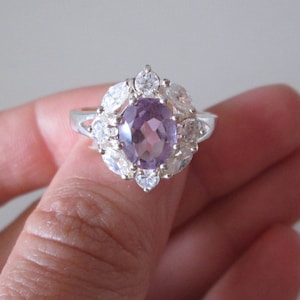 May include: A silver ring featuring a large oval amethyst gemstone surrounded by smaller clear gemstones.