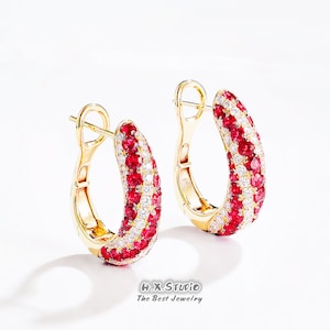 Puede incluir: Un par de pendientes de aro de oro con un diseño rojo y blanco. Los pendientes están engastados con pequeñas piedras preciosas rojas y blancas.