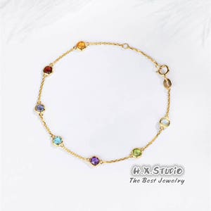 May include: A gold chain bracelet featuring seven colourful gemstones. The gemstones are arranged in a rainbow order, starting with red and ending with purple. The bracelet has a lobster clasp fastening.