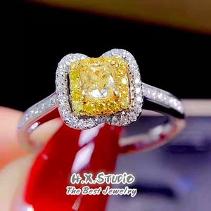 May include: A yellow diamond engagement ring with a square-shaped center stone surrounded by smaller diamonds. The ring is set in white gold and has a delicate band.
