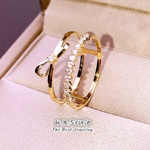 May include: Gold ring with a double band design. One band features a bow with clear cubic zirconia stones. The other band has a row of clear cubic zirconia stones.
