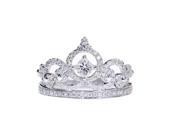 May include: A silver crown ring with a large square-shaped diamond in the center and smaller diamonds surrounding it.