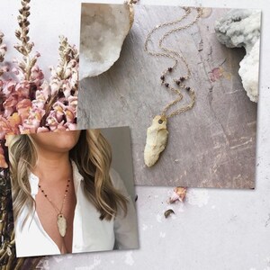 May include: A gold chain necklace with a brown stone pendant and small red beads. The pendant is a long, thin, pointed stone.