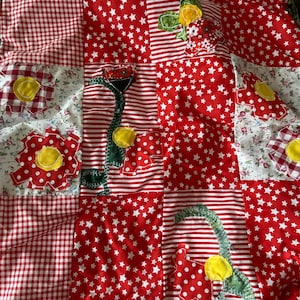 May include: A patchwork quilt with a variety of patterns. Red and white gingham, red and white striped, and red fabric with white stars are used. Appliqued flowers and other shapes with yellow centers and green leaves are sewn onto the quilt.