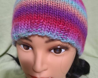 May include: A colorful striped knitted hat in shades of pink, purple, blue, and teal. The hat is made with a soft yarn and has a simple, classic design.