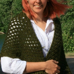 May include: A woman wearing a white shirt and a green crocheted shawl with white accents. The shawl is draped over her shoulders and tied at the front.