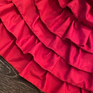 May include: A close-up of a red fabric skirt with multiple layers of ruffles. The ruffles are sewn with a zig-zag stitch.