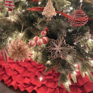 May include: A red ruffled Christmas tree skirt with a green Christmas tree decorated with ornaments, including a white ceramic tree, red and white striped candy cane ornaments, a gold snowflake, and a red wire ball ornament.