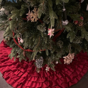 May include: A red ruffled Christmas tree skirt with multiple layers of ruffles. The skirt is placed on a wooden floor.