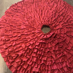 May include: A full circle burgundy red skirt with multiple layers of ruffles. The skirt is made of a soft, flowing fabric.