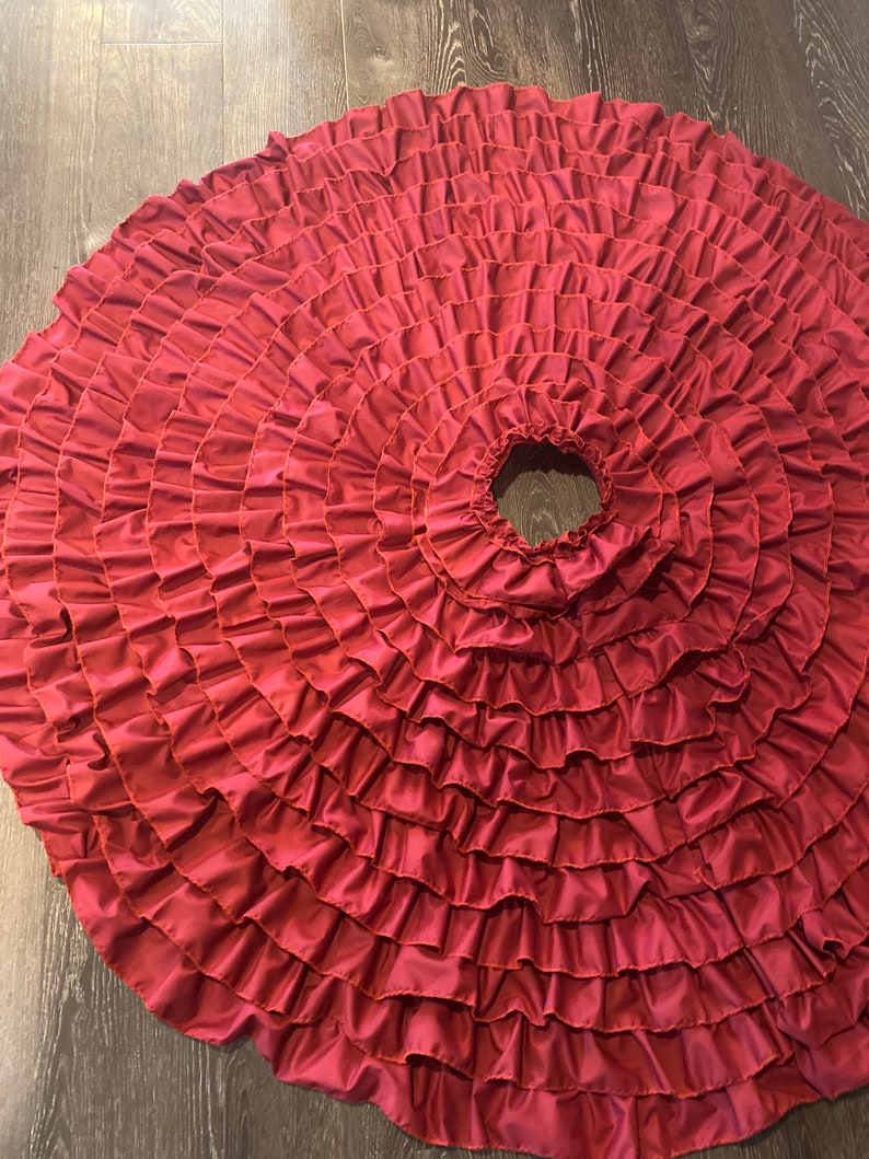 May include: A full circle burgundy red skirt with multiple layers of ruffles. The skirt is made of a soft, flowing fabric.