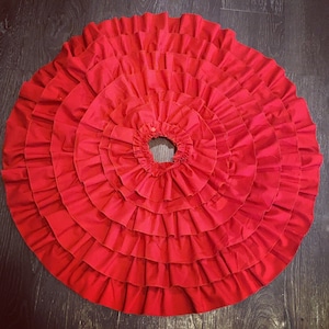 May include: A red ruffled skirt with multiple layers of fabric. The skirt is circular and has a center hole.