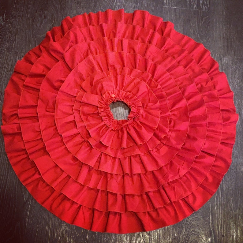 May include: A red ruffled skirt with multiple layers of fabric. The skirt is circular and has a center hole.