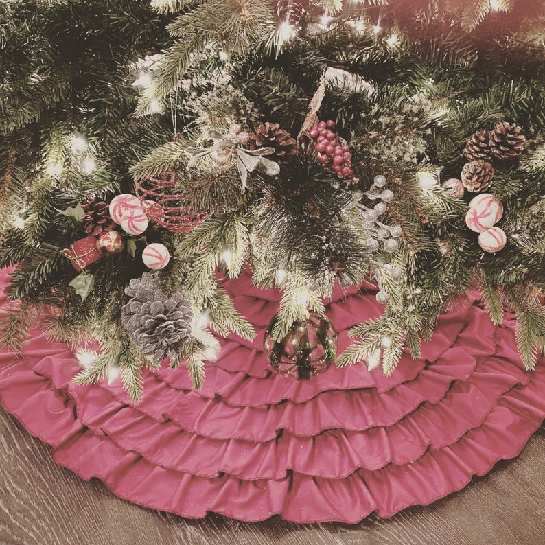 May include: A pink ruffled Christmas tree skirt with a green Christmas tree decorated with ornaments, candy canes, and pine cones.