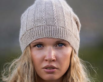 May include: A light beige knit beanie with a ribbed brim and vertical textured panels. The hat is made of a soft, warm material, perfect for cold weather. The beanie is a neutral color, making it versatile for various outfits.