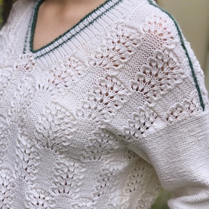 Puede incluir: Suéter de crochet blanco con ribete verde alrededor del cuello y los hombros.
