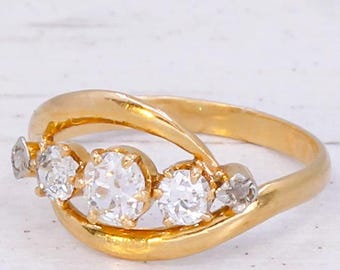 May include: A gold ring featuring five clear gemstones. The ring has a curved design with the gemstones set in a row. The band is a bright gold color, and the gemstones sparkle against the gold.