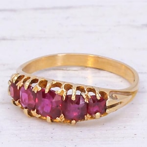Könnte beinhalten: Ein Goldring mit fünf roten Edelsteinen, die in einem dekorativen, durchbrochenen Design gefasst sind.