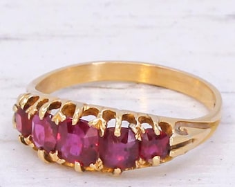 May include: A gold band ring with five red gemstones set in a decorative, openwork design.