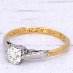 May include: A gold and silver engagement ring with a round diamond. The band is inscribed with "MARY - ALEX".