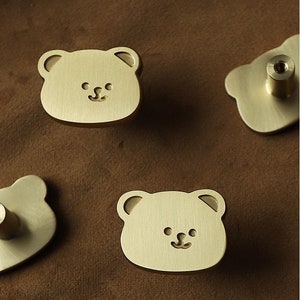 May include: Four gold-toned bear-shaped cabinet knobs with a simple smiling face design.