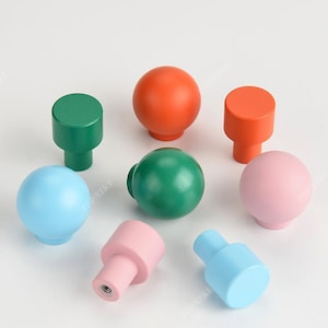 Op de afbeelding: Assortiment van kleurrijke houten knoppen in verschillende vormen, waaronder ronde en cilindrische. De knoppen zijn in tinten blauw, groen, roze en oranje.