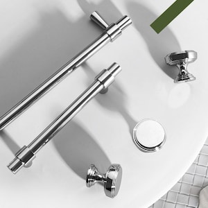 Op de afbeelding: Een set van vier gepolijste chromen kastbeslag, waaronder twee lange stanggrepen en twee ronde knoppen. Het beslag heeft een modern, minimalistisch ontwerp.