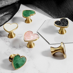 Puede incluir: Conjunto de seis pomos de armario en forma de corazón con base de latón y incrustaciones de diferentes colores. Las incrustaciones incluyen blanco, rosa, verde y negro.