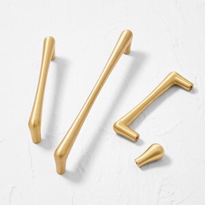 May include: Four gold-toned cabinet pulls in different sizes and shapes. The pulls have a brushed finish and are made of metal.