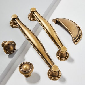 May include: Set of five antique brass cabinet hardware pulls with a beaded edge. The set includes two long pulls, two small knobs, and one arched pull.