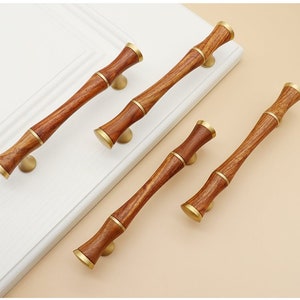 Puede incluir: Conjunto de cuatro tiradores de armario de madera con diseño de bambú y detalles dorados. Los tiradores son de diferentes tamaños.
