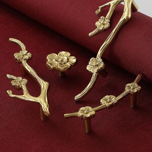 以下が含まれることがあります： 花柄の金色のキャビネットノブが4つ。ノブは枝と花の形をしています。