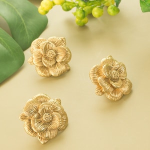 May include: Three gold-tone flower-shaped earrings. The earrings are made of metal and have a textured surface.
