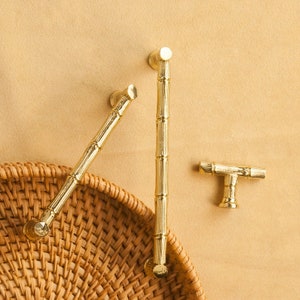 May include: Three gold-toned cabinet knobs with a bamboo design. The knobs are on a light brown background.