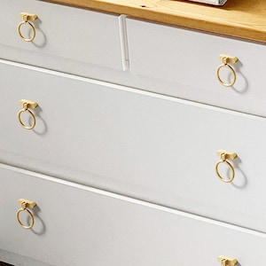 May include: White chest of drawers with five drawers and gold ring-shaped handles.