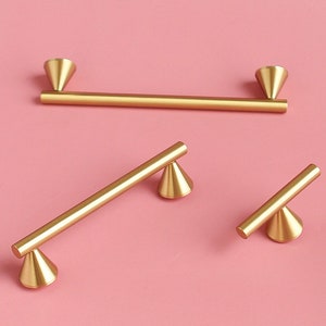 May include: Three gold metal cabinet pulls with a cone-shaped design on each end. The pulls are different sizes.