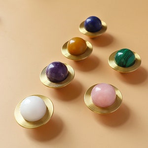 Puede incluir: Seis pomos decorativos para armarios con base de metal dorado y parte superior redonda de piedra preciosa. Las piedras preciosas son amatista, malaquita, lapislázuli, cuarzo rosa, ágata blanca y citrino.