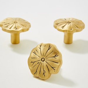 May include: Three gold-toned cabinet knobs with a lotus flower design. The knobs have a raised, textured surface and a circular base.