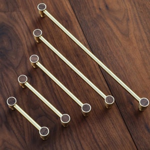 May include: Five gold cabinet pulls with wooden knobs. The pulls are arranged in a diagonal line on a wooden surface.