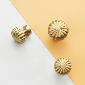 May include: Three gold-toned cabinet knobs with a fluted design. The knobs are round and have a slightly raised centre.