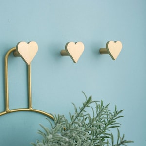 May include: Three gold heart-shaped hooks mounted on a light blue wall. The hooks are part of a decorative wall rack.