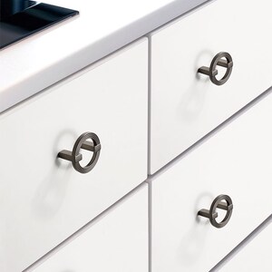 以下が含まれることがあります： 円形のデザインと長方形のバーが付いた3つの引き出しの取っ手のクローズアップ。引き出しの取っ手は、ブラッシュドニッケル仕上げです。