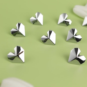 May include: Eight silver origami hearts on a light green background. The hearts are folded into a geometric shape with sharp points.