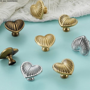 May include: Assortment of heart-shaped cabinet knobs in gold and silver finishes. The knobs have a ribbed design and are perfect for adding a touch of elegance to any room.