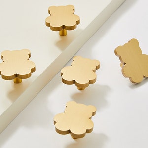 Op de afbeelding: Vijf gouden, beren-vormige kastknoppen. De knoppen hebben een glad, afgerond oppervlak en een eenvoudig, minimalistisch ontwerp.